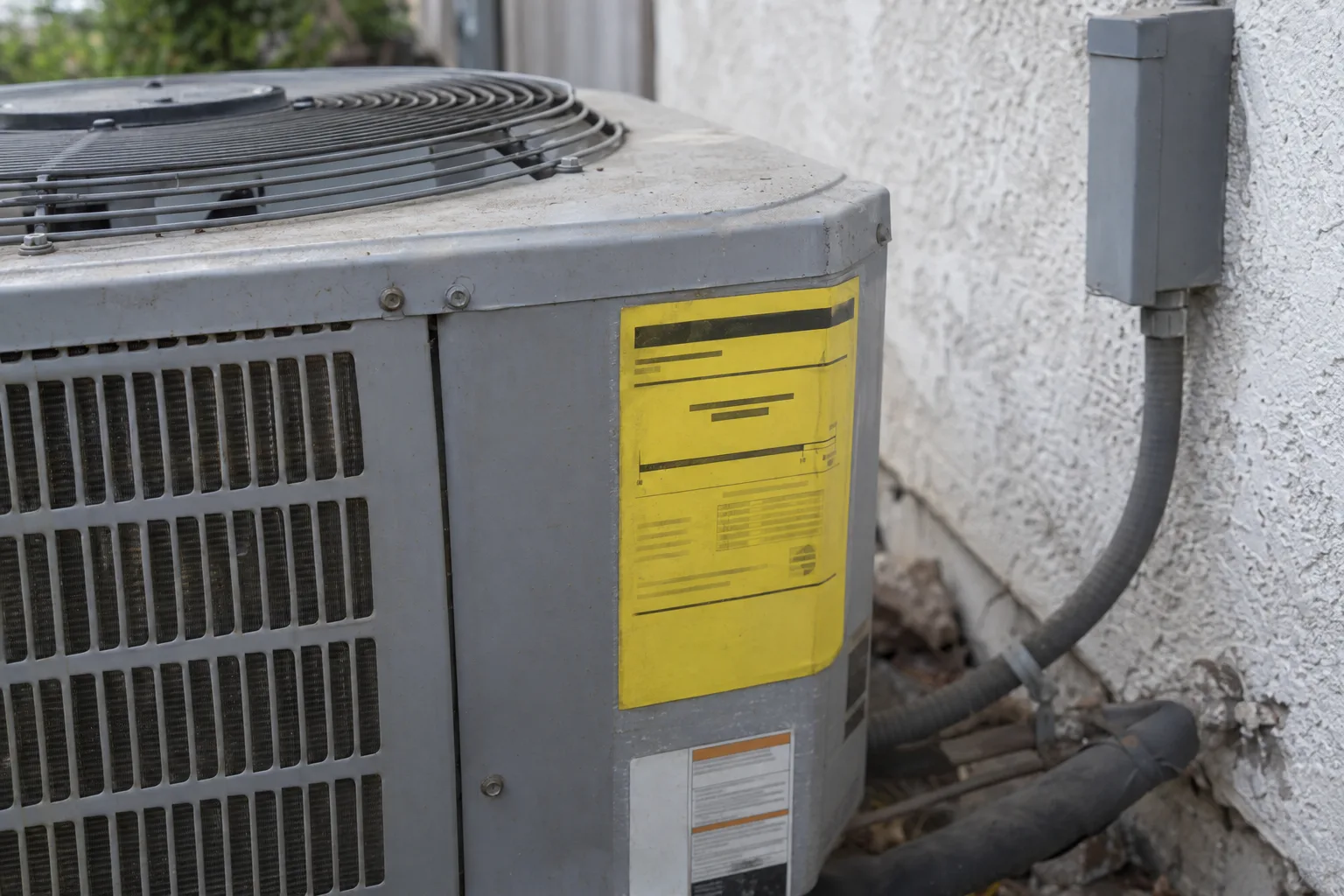 Close-up of a yellow EnergyGuide efficiency placard on a newly installed air conditioner condenser, mounted against a white stucco exterior wall in soft afternoon California light.