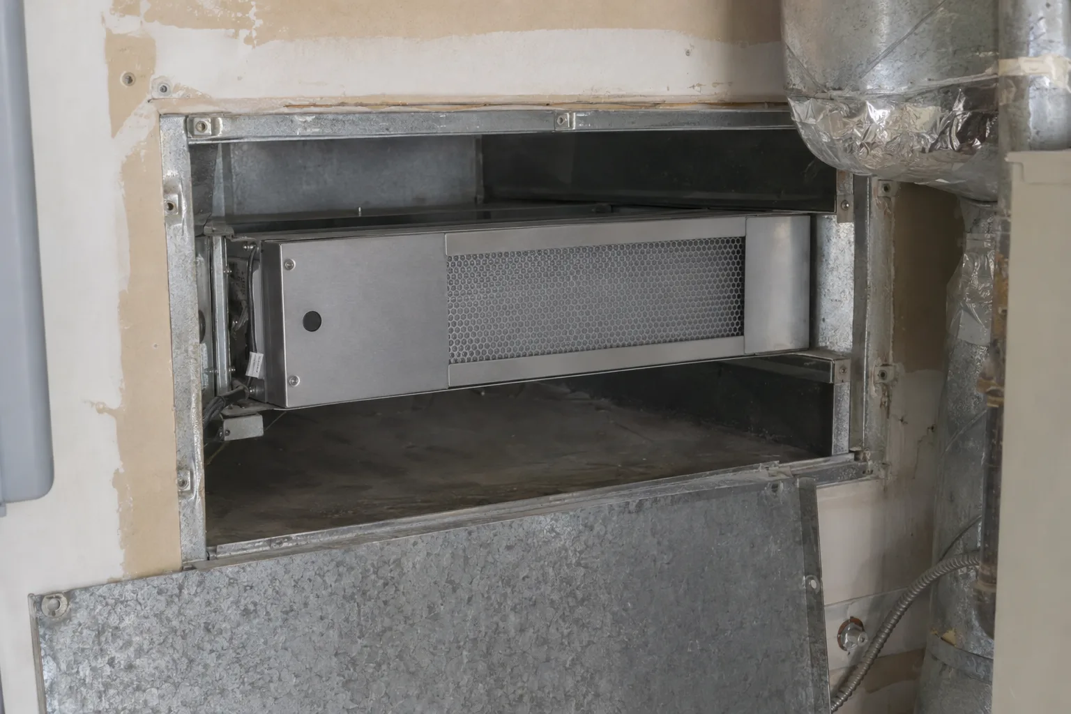 An in-duct whole-home air purifier unit installed inside a residential HVAC supply duct, visible through an open access panel on a utility room wall