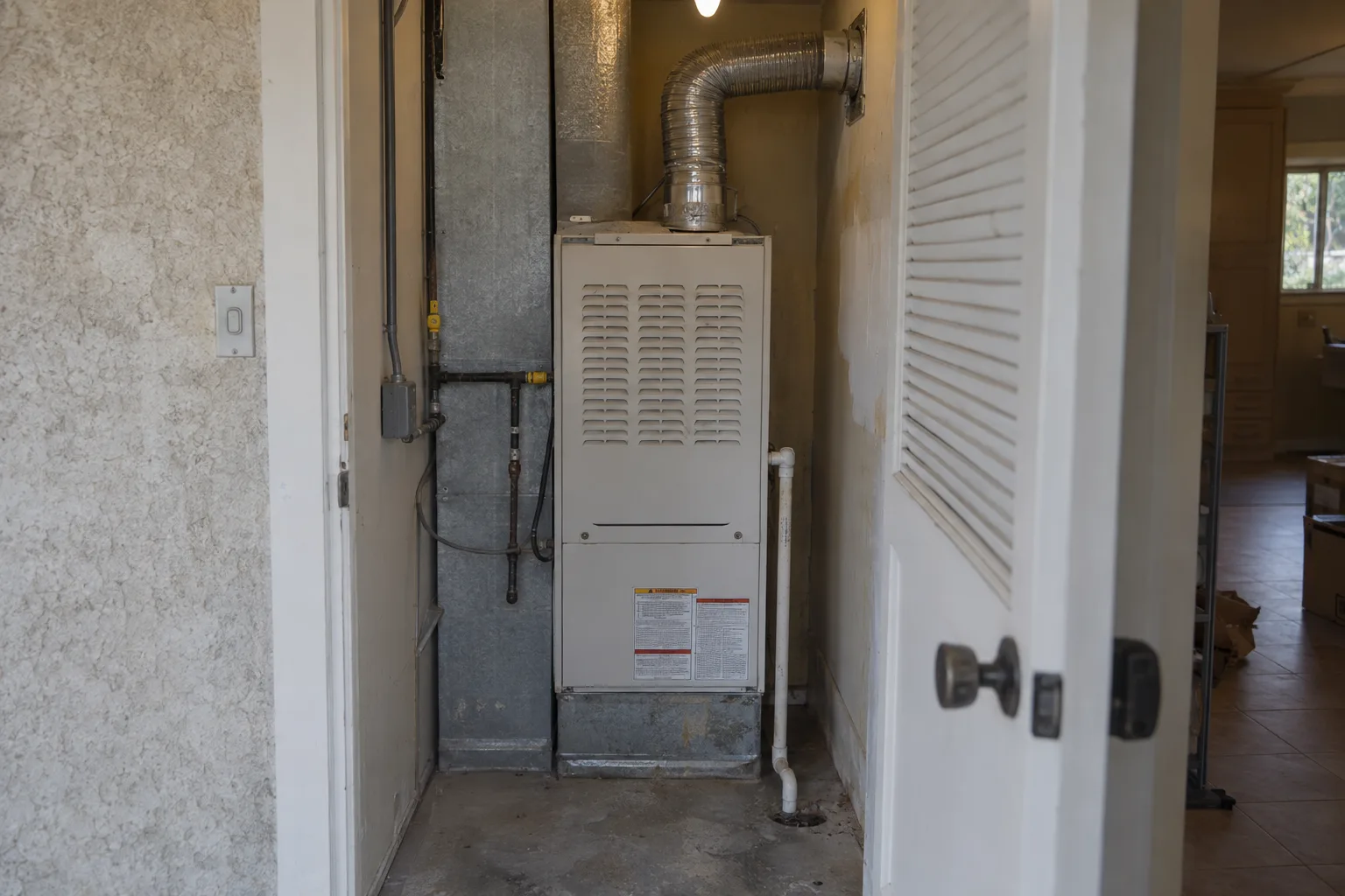 A high-efficiency gas furnace installed in a utility closet of a Southern California ranch home, showing the white cabinet unit, flue pipe, and condensate drain line.