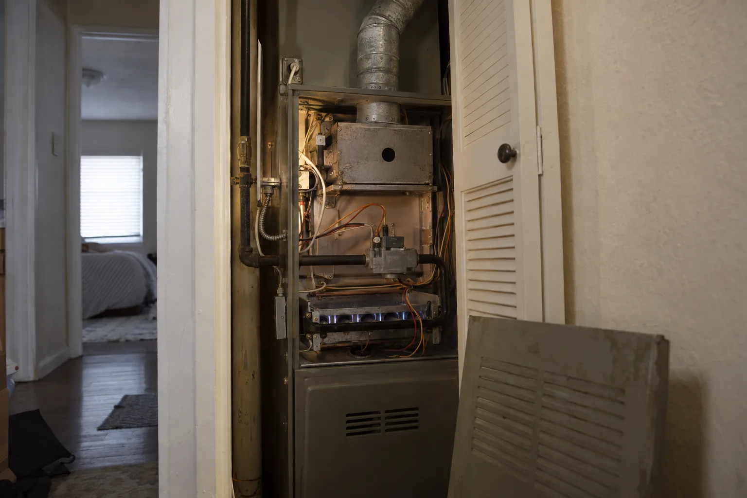 Interior of a residential furnace closet with the access panel removed, exposing the burner assembly and heat exchanger of an upright gas furnace installed in a Los Angeles home