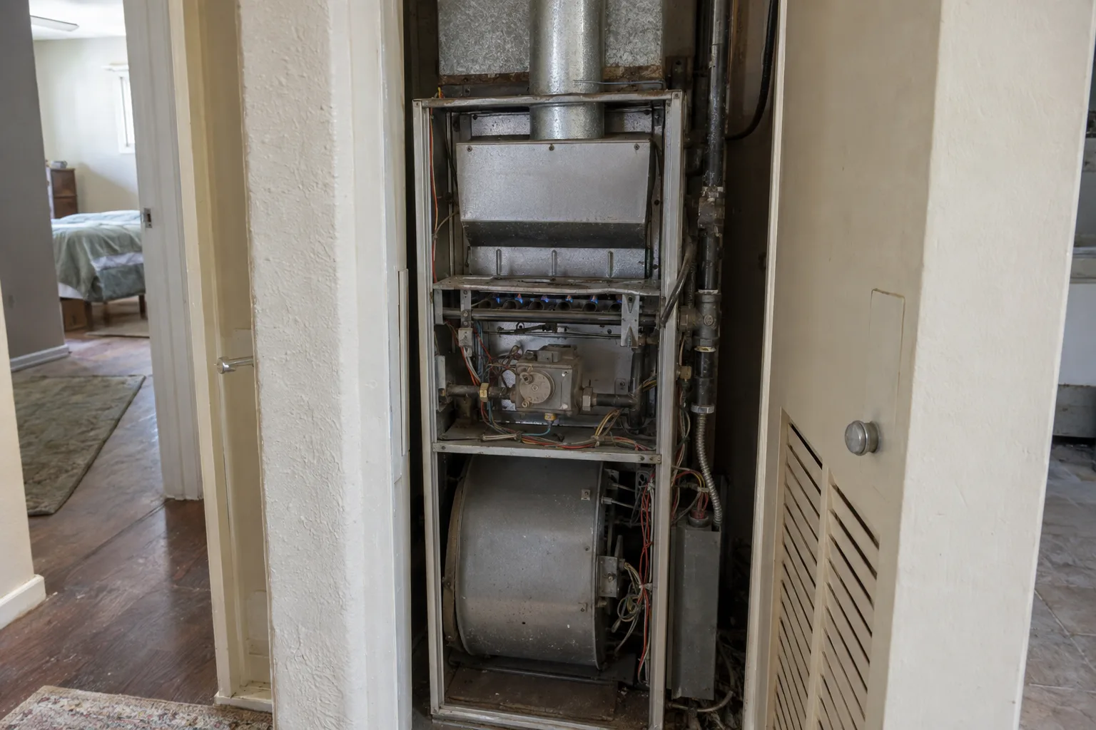 A residential forced-air furnace with its access panel removed, exposing the heat exchanger, burner assembly, and blower compartment inside a utility closet