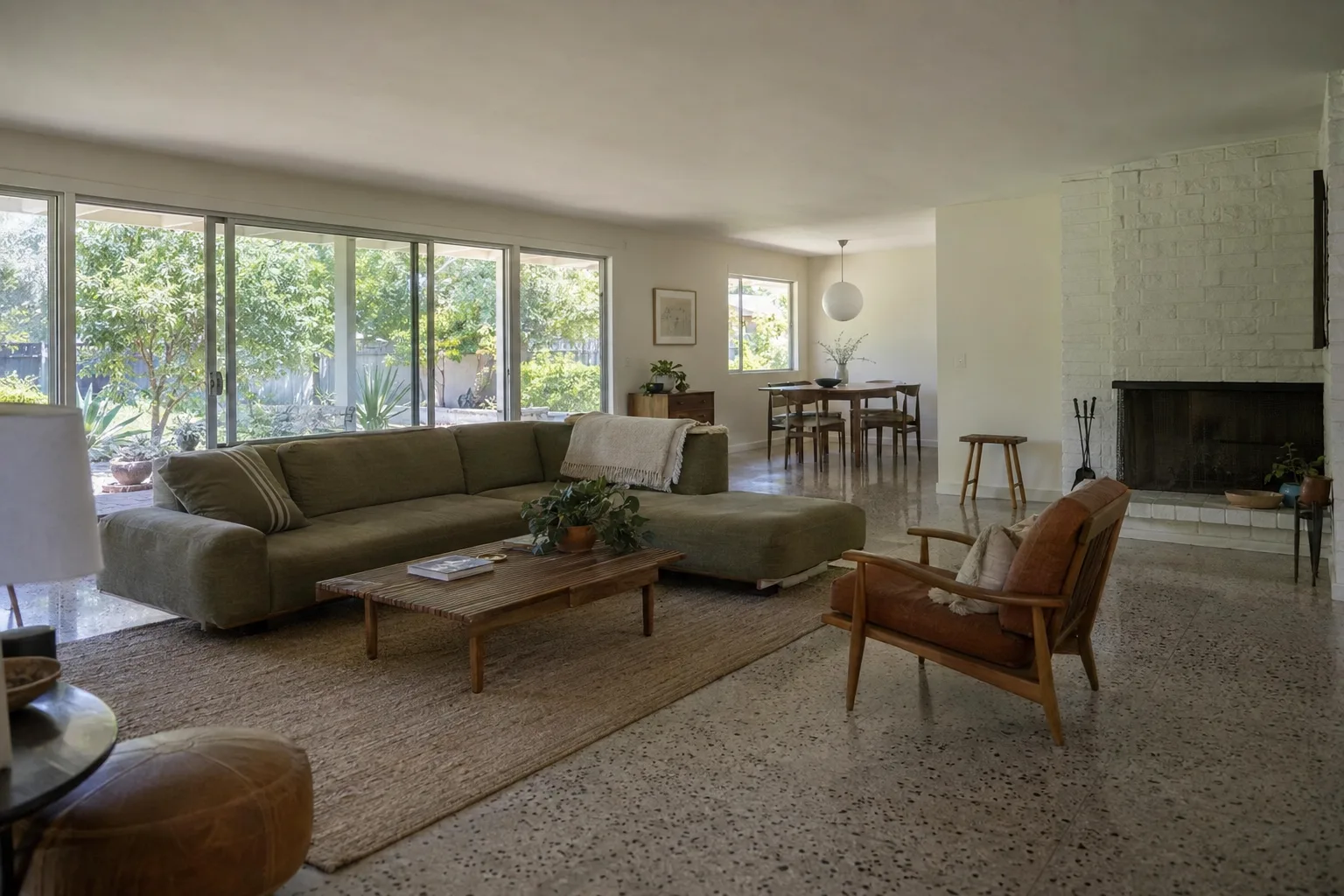 Sunlit open-plan living room in a mid-century ranch home with terrazzo floors, low furniture, and warm California daylight streaming through sliding glass doors