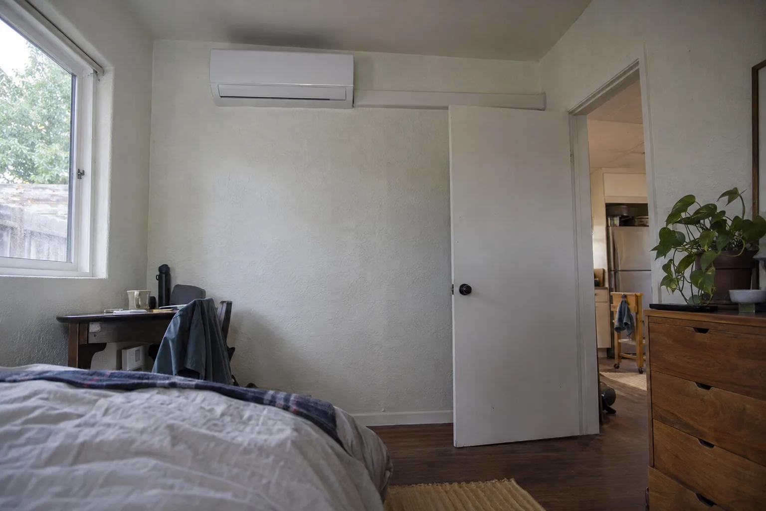 A wall-mounted ductless mini-split indoor head unit installed high on a white stucco wall inside a small Los Angeles ADU, with a tidy line-set cover running down the wall
