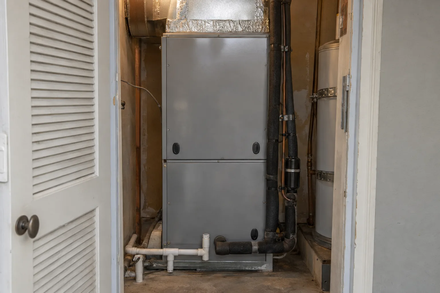 Variable-speed air handler unit installed vertically in a residential utility closet, with insulated refrigerant lines and ductwork connections visible